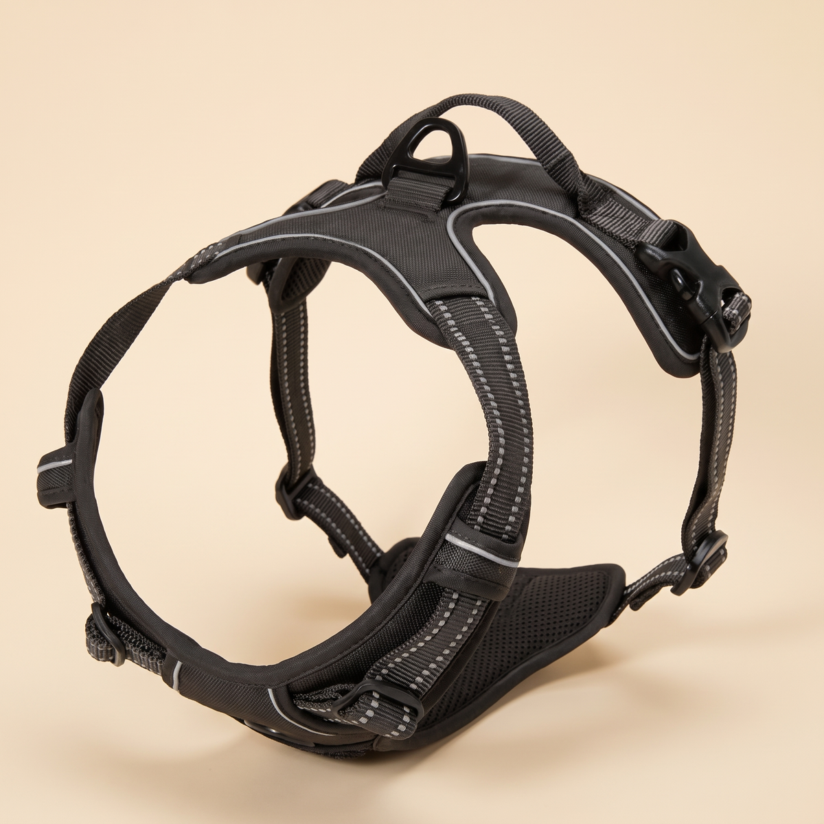 Black reflective no pull dog harness with padded chest and back plates on a plain cream background
