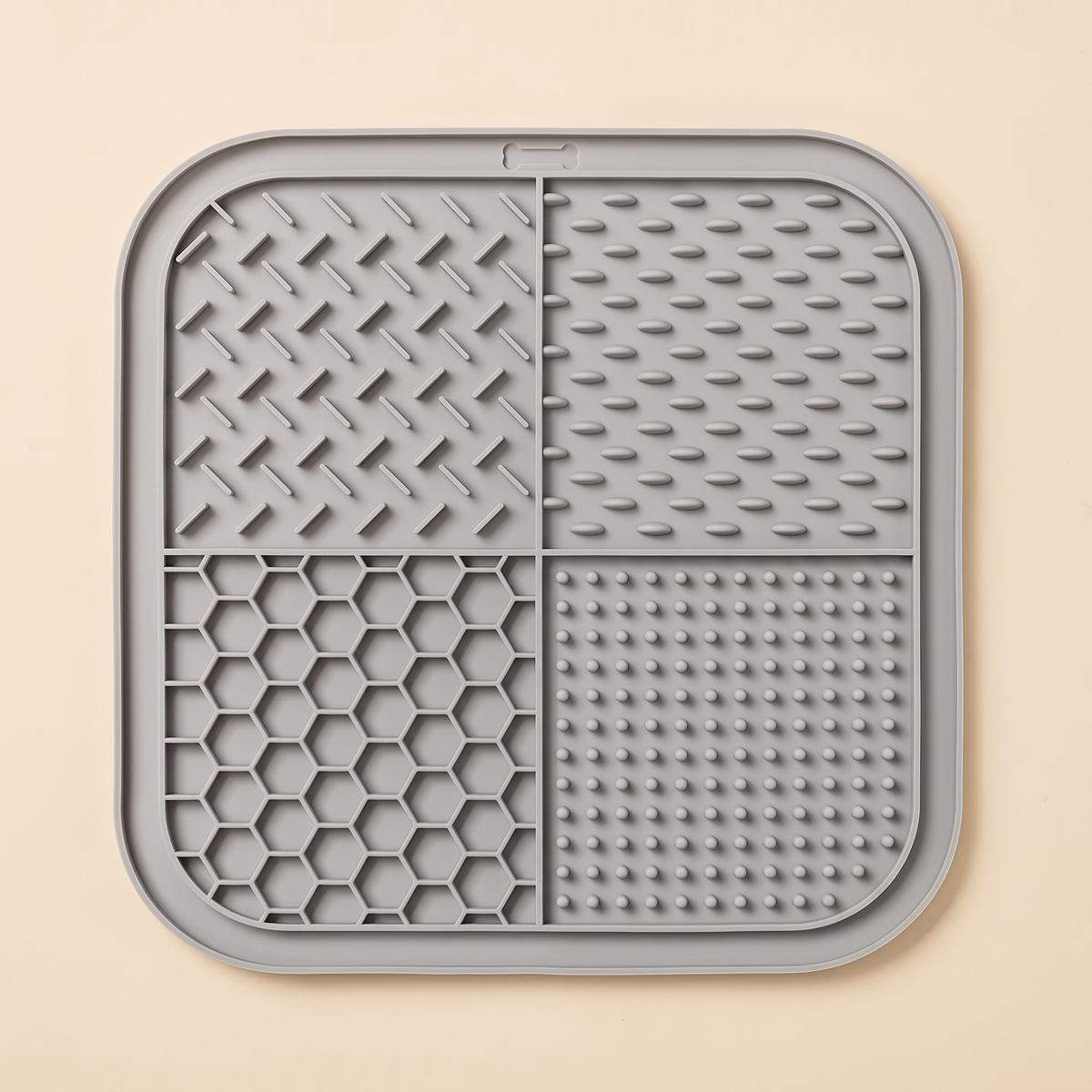 Square grey silicone lick mat with four different textures on a plain cream background