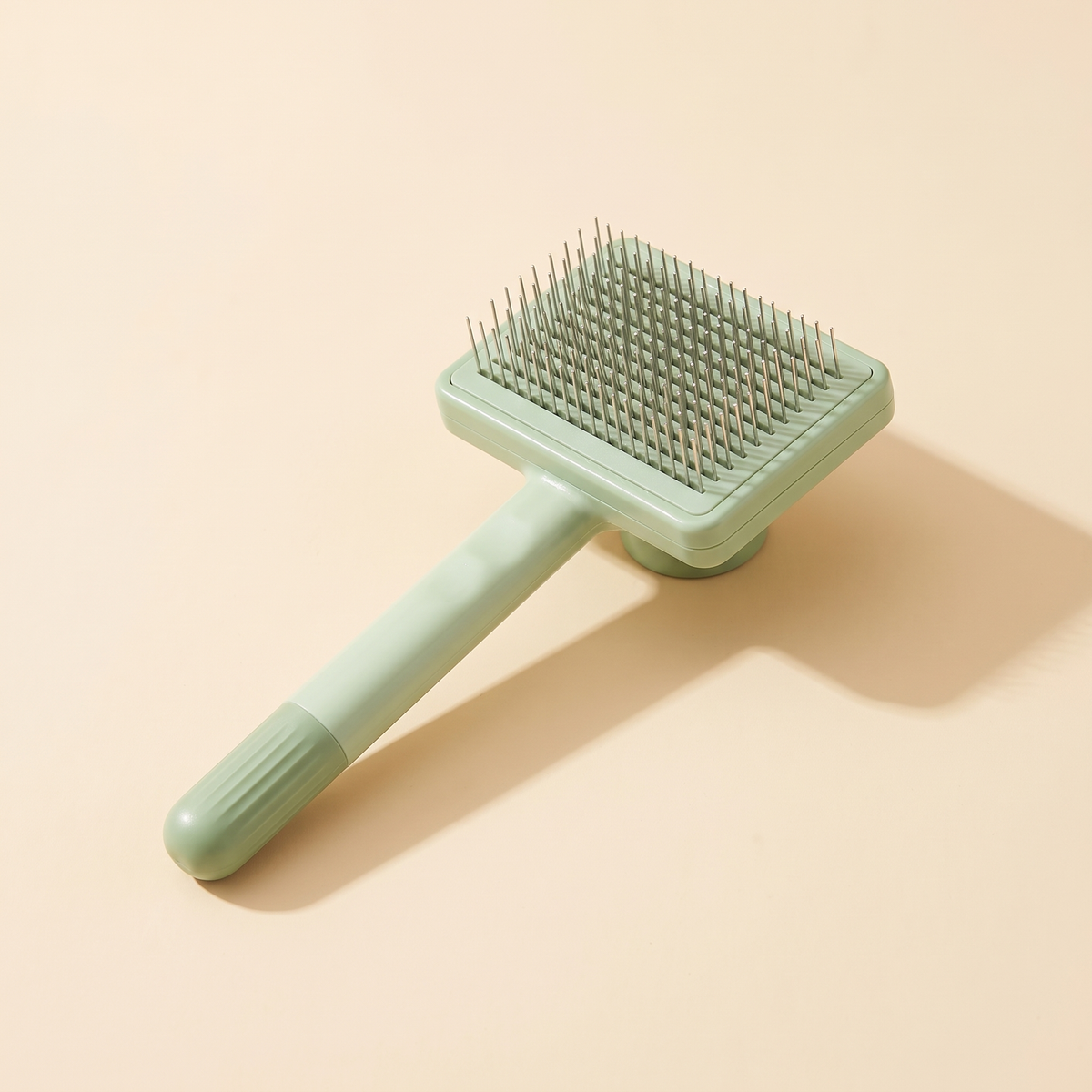 Sage green self cleaning cat and dog grooming brush on a plain cream background