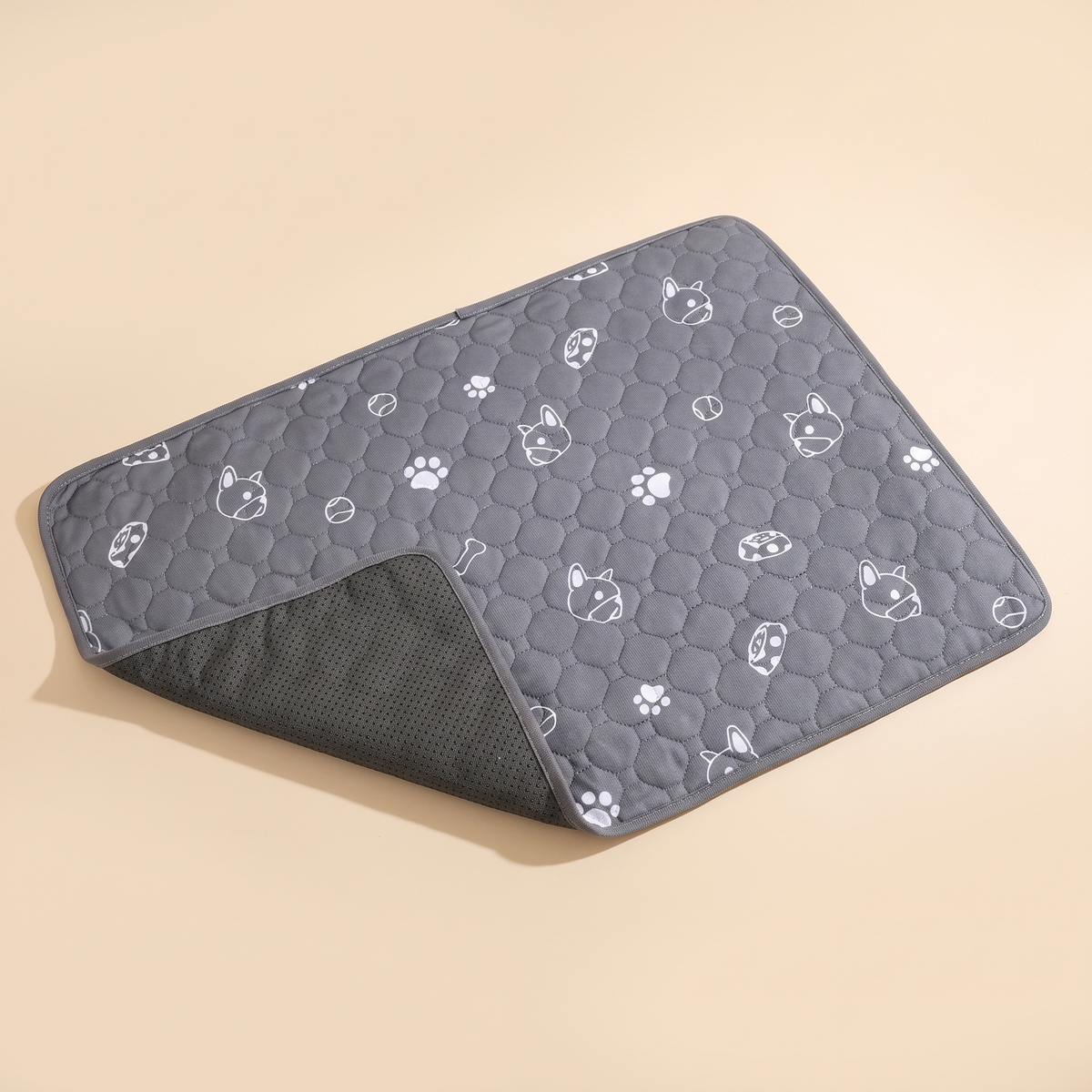 Grey quilted washable puppy pee pad with one corner folded back on a plain cream background