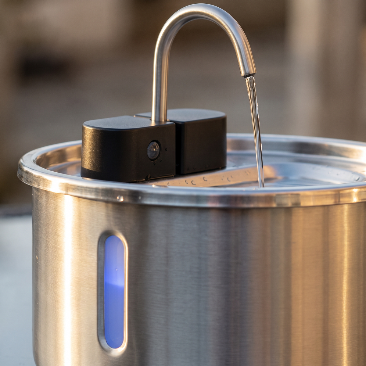 Close-up of the stainless steel spout, black sensor module and blue water level window on the 7L pet fountain