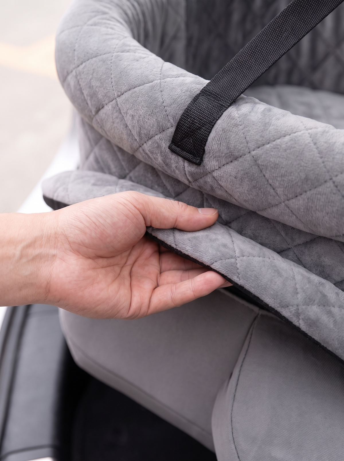 Close detail of the quilted grey cover being lifted from the pet car booster seat