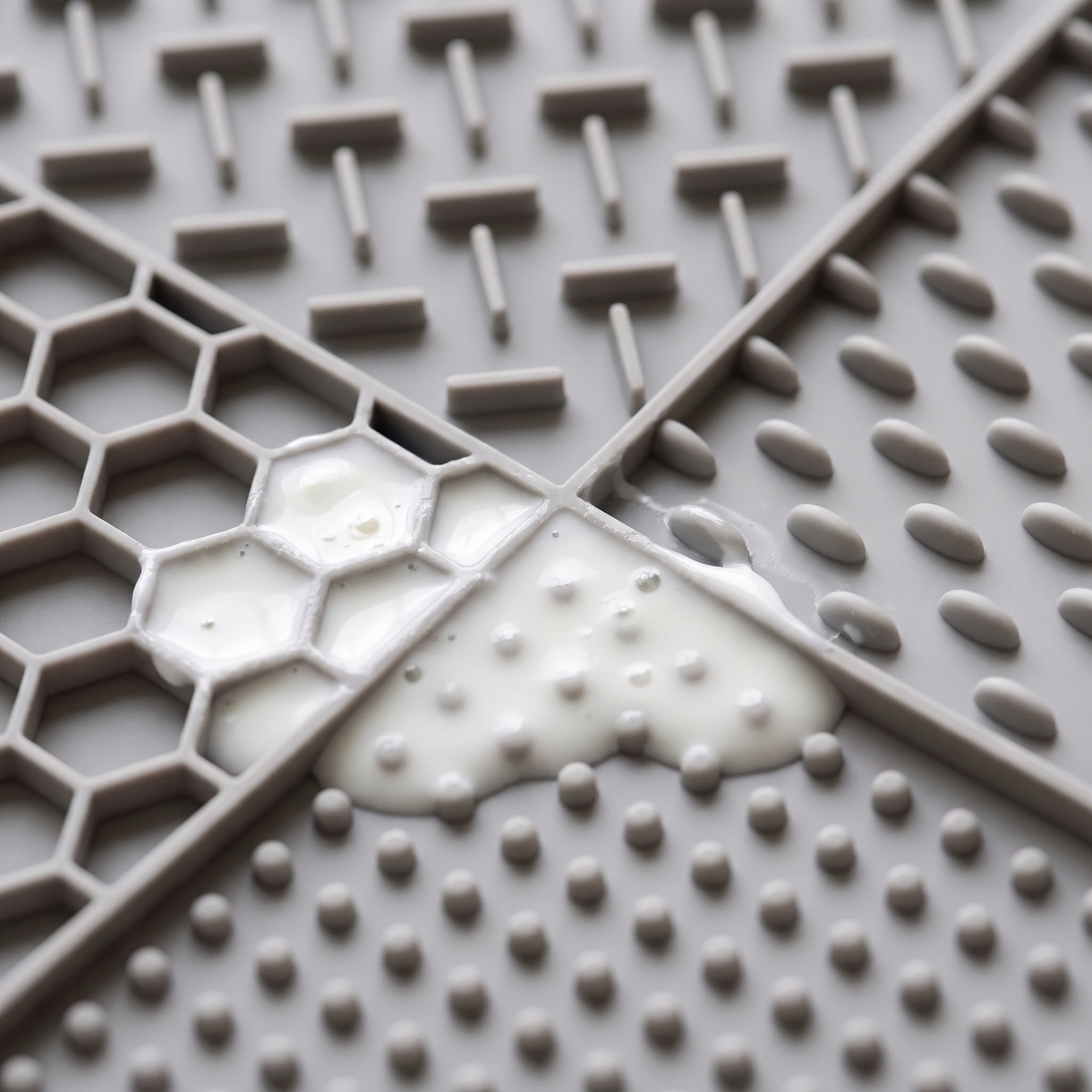 Close-up of yoghurt pressed into the honeycomb and dotted textures of the grey lick mat