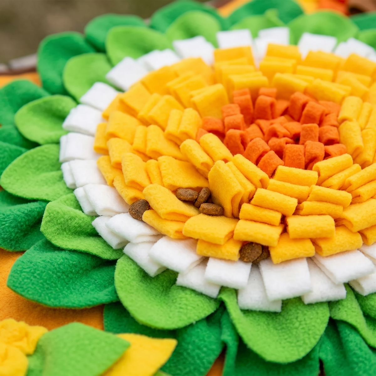 Close-up of kibble hidden among the yellow, orange and white fleece petals of the snuffle mat