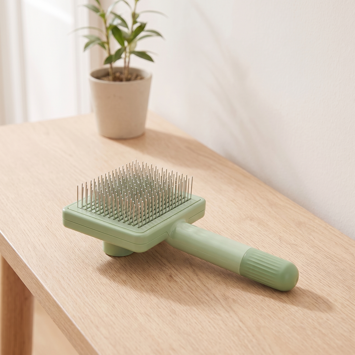 Sage green self cleaning pet grooming brush with steel pins lying on an oak console table