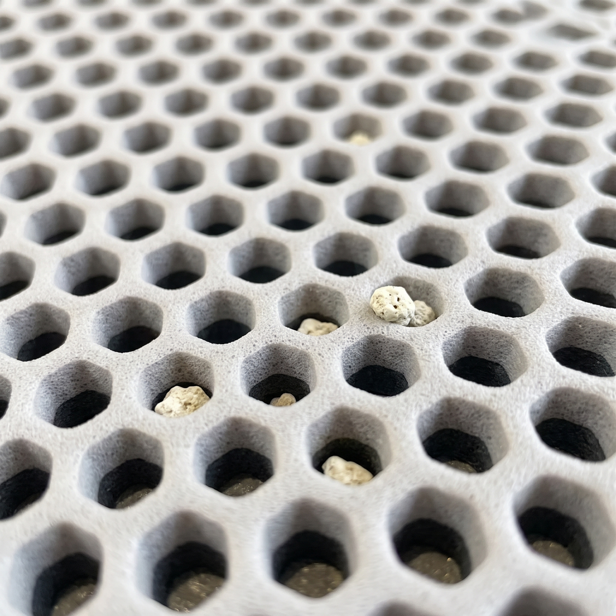 Close-up of litter granules caught in the honeycomb holes of the grey litter mat