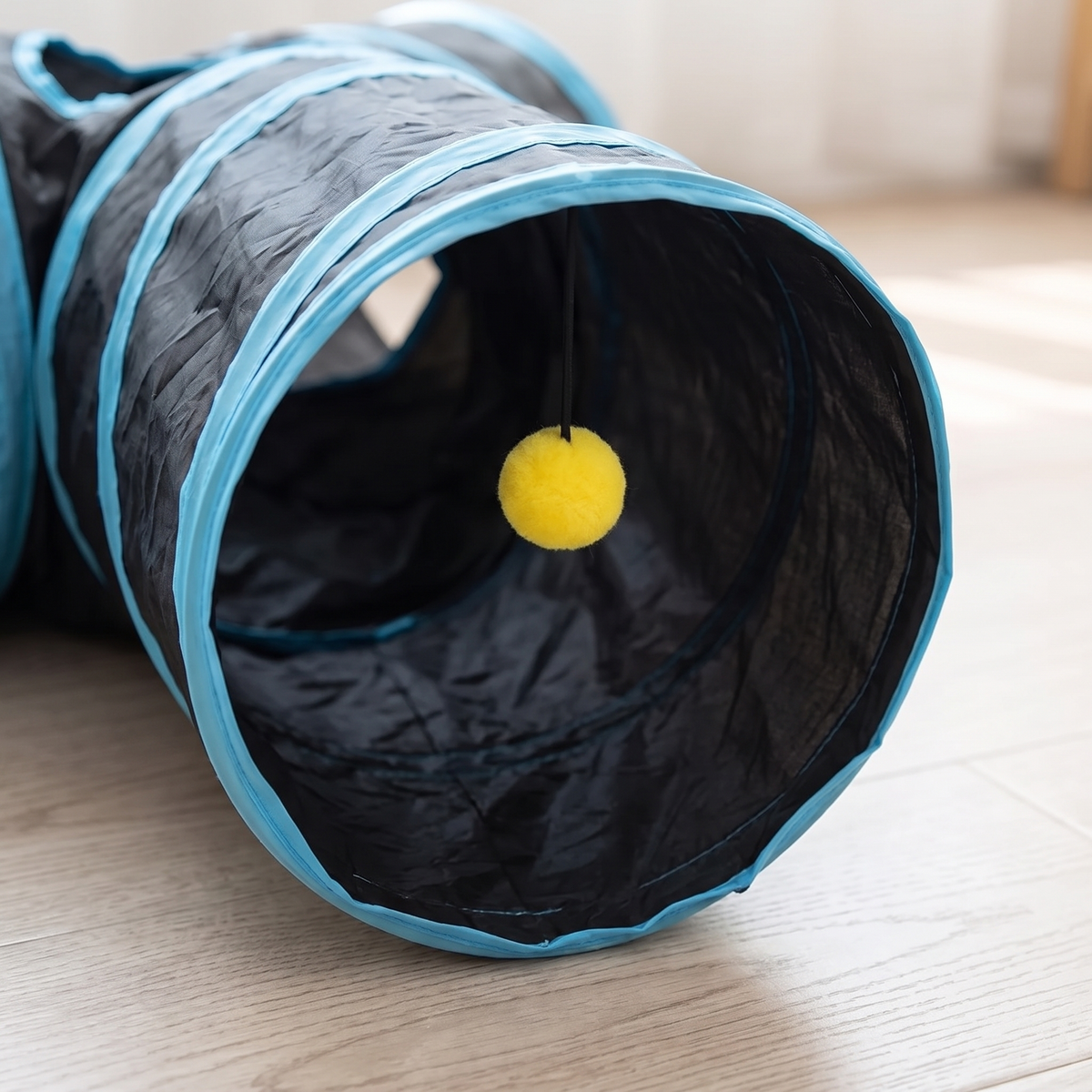 Close-up of the blue rim and hanging yellow ball at an opening of the cat tunnel