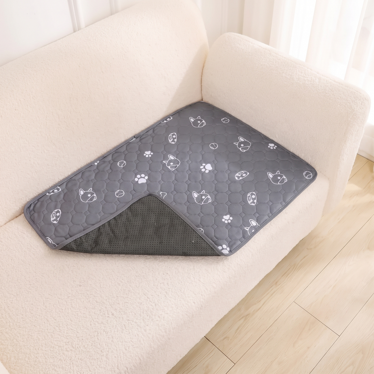 Grey washable puppy pad with white paw and puppy print laid on a cream sofa seat