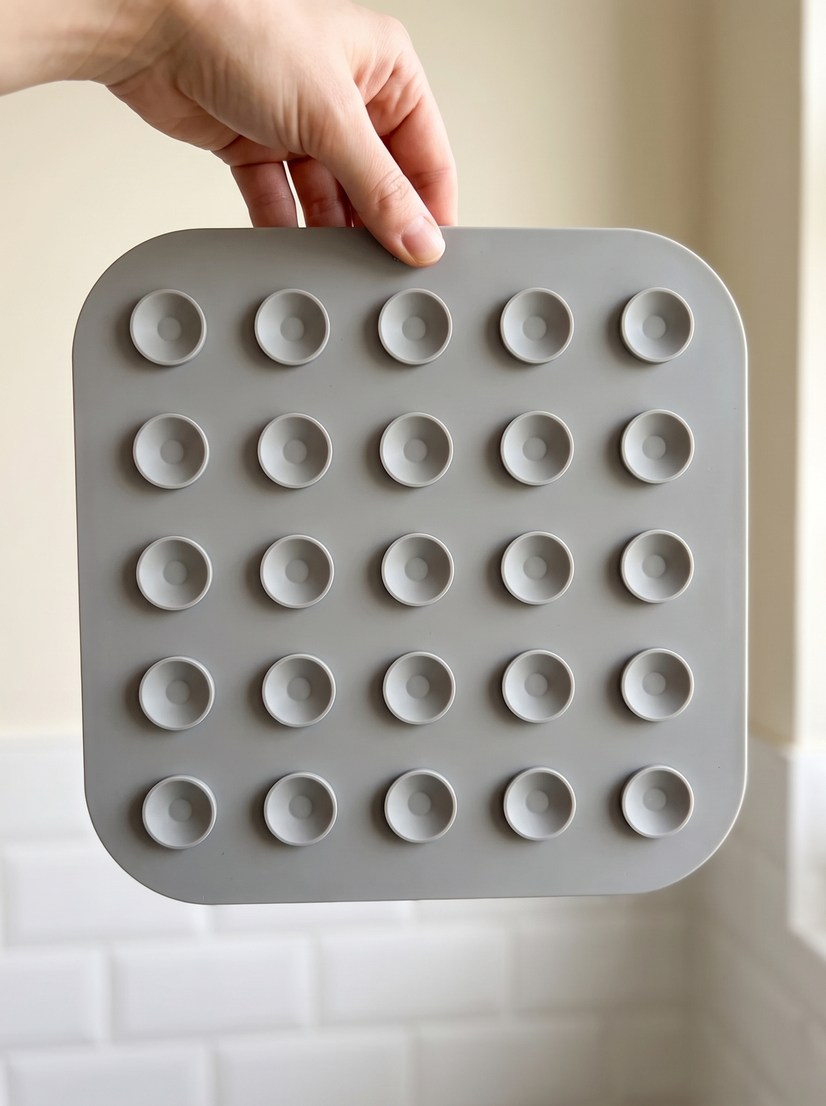 Hand holding the grey lick mat to show the grid of suction cups on the back