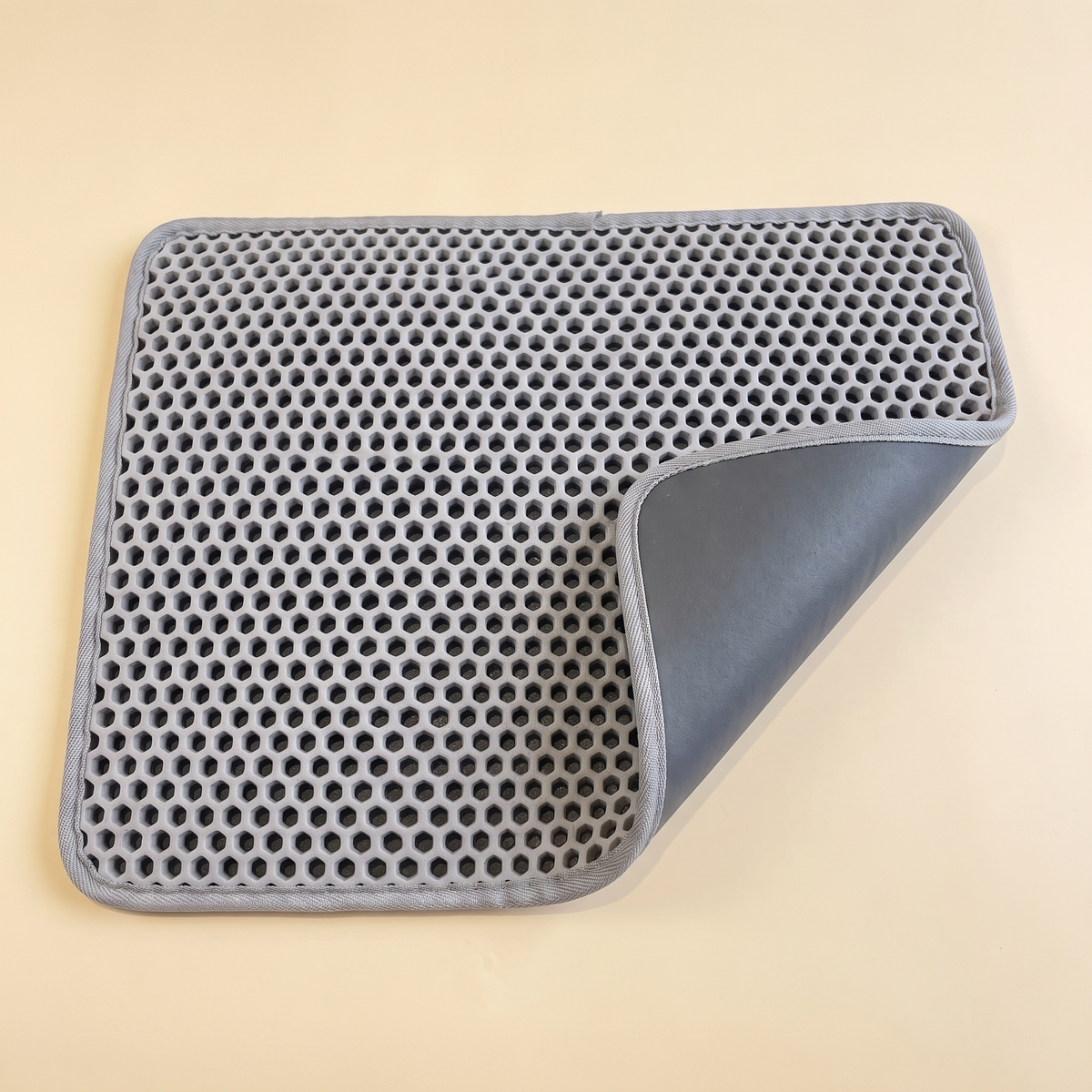 Grey double layer honeycomb cat litter mat with one corner curled back on a plain cream background