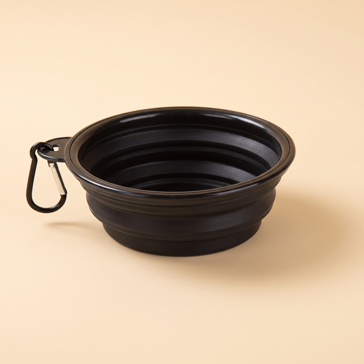 Black collapsible silicone dog travel bowl with carabiner on a cream background