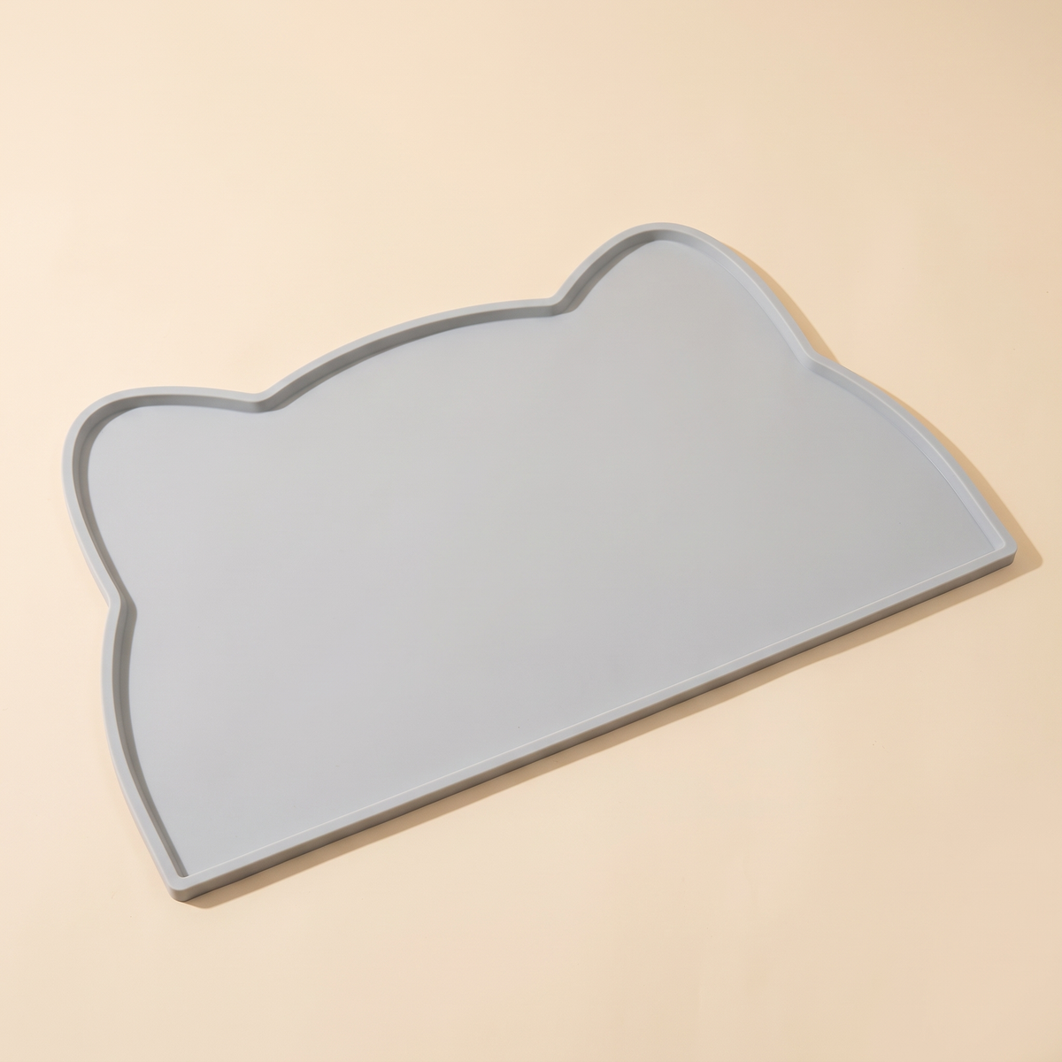 Grey cat-shaped silicone pet feeding mat with raised edge on a cream background