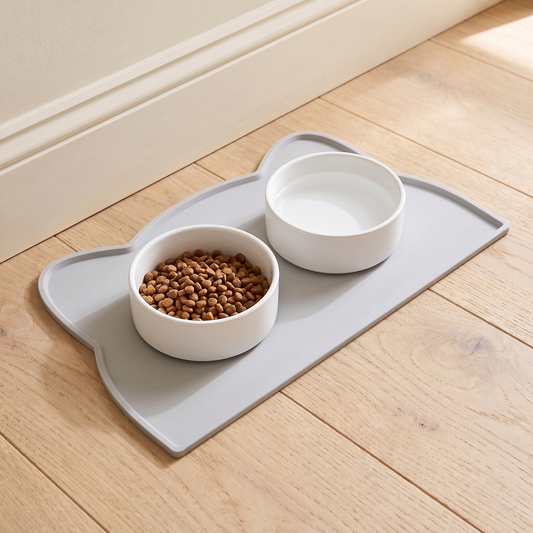 Grey silicone pet feeding mat with two white bowls on an oak kitchen floor