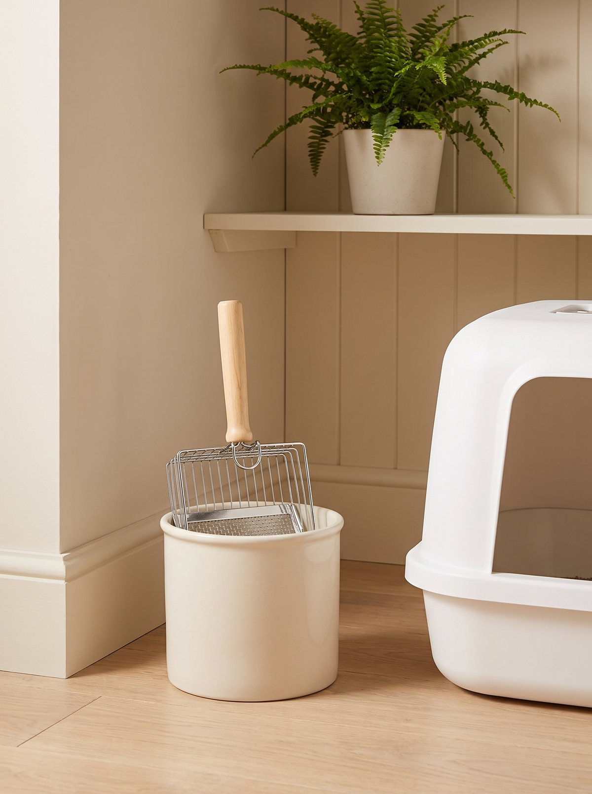 Stainless steel litter scoop stored in a ceramic pot beside a litter box