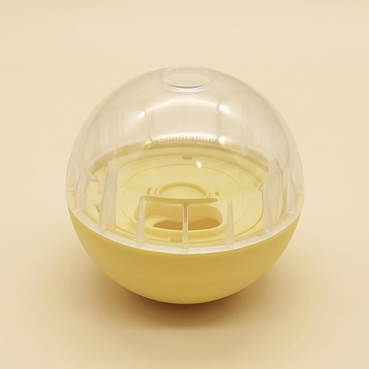 Yellow and clear dog treat dispensing ball on a cream background