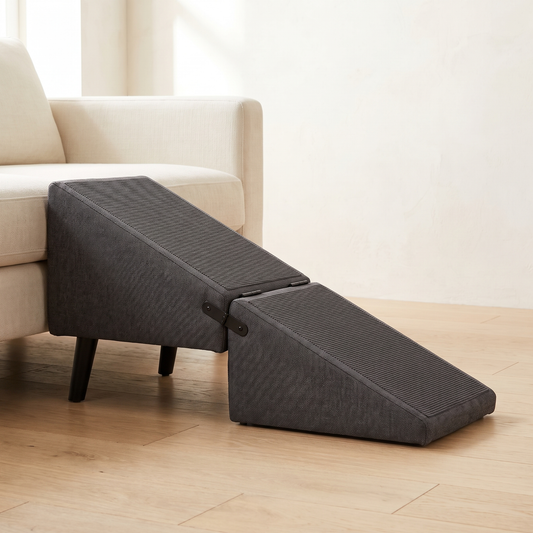 Charcoal grey folding dog ramp opened in front of a low cream sofa, on black tapered legs
